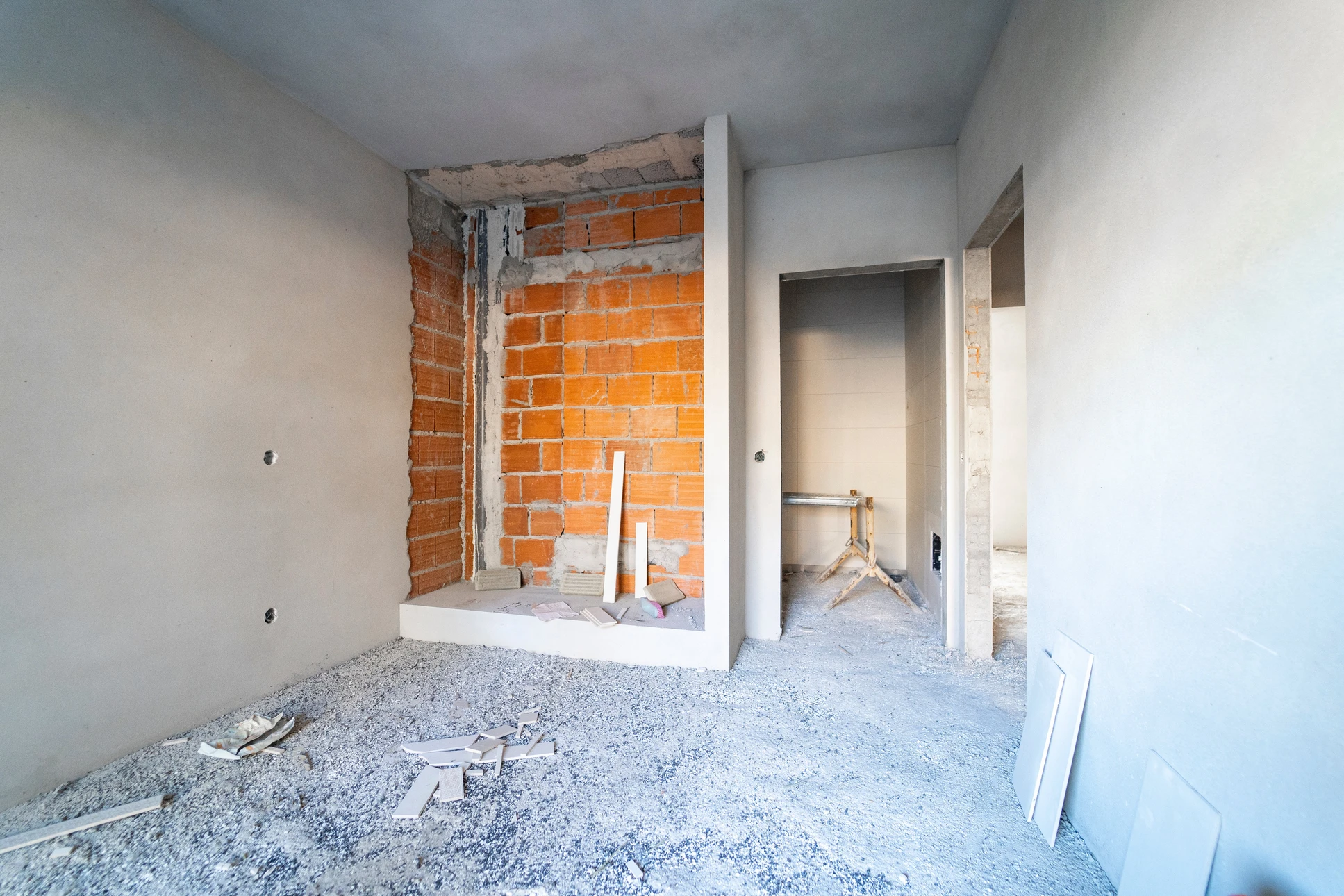 Chantier de rénovation intérieure avec murs en briques apparentes partiellement démolis, cloisons en plaques de plâtre en cours d'installation