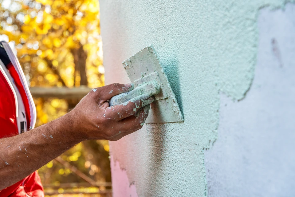 Ouvrier en équipement de protection individuelle appliquant de la peinture sur façade extérieure d'immeuble